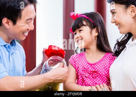 Famiglia cinese di risparmio di denaro per college fund del bambino, mettendo le monete in vaso Foto Stock