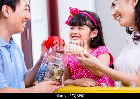 Famiglia cinese di risparmio di denaro per college fund del bambino, mettendo le monete in vaso Foto Stock