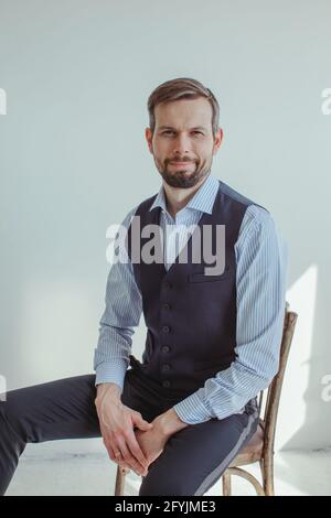 Ritratto di un uomo sorridente in una camicia e gilet seduto su una sedia Foto Stock