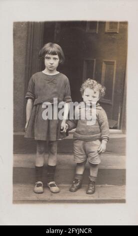 Cartolina fotografica britannica vintage dei primi del XX secolo che mostra due poveri, e triste guardare bambini tenendo le mani. Foto Stock