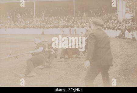 Cartolina fotografica d'epoca dei primi del XX secolo che mostra uno stadio pieno di spettatori che guardano un gruppo di uomini di guerra. Foto Stock