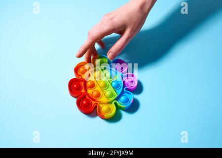 La ragazza si allunga con la sua mano a colorful trendy pop esso giocattolo in forma di fiore su sfondo blu. Vista dall'alto, disposizione piatta Foto Stock