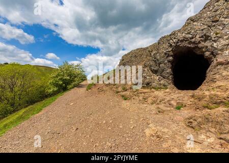 L'ingresso alla grotta di Clutter's Cave nelle colline di Malvern con il campo britannico sullo sfondo, Worcestershire, Inghilterra Foto Stock