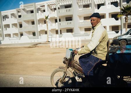 ESSAOUIRA, MAROCCO - 17 GENNAIO 2020: L'uomo marocchino in camicia sporca cavalca un triciclo. I Benin soffrono di povertà a causa della cattiva economia. Contrassegno locale Foto Stock