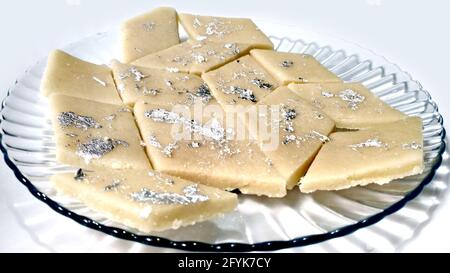 Il Kaju Katli è un dolce indiano a forma di diamante fatto usando lo zucchero di anacardi e la mava, servito in un piatto isolato su sfondo bianco. Fuoco selettivo Foto Stock