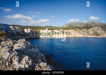 Costa occidentale dell'isola di Cefalonia. Assos villaggio sul retro. Bellissima baia blu con rocce calcaree marroni Grecia Foto Stock