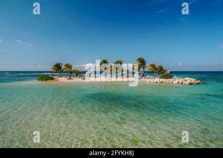 Piccola e bella isola paradiso per turisti con palme, spiaggia, grandi pietre e lettini da spiaggia per prendere il sole. Sogno di destinazione caraibica. Un Foto Stock