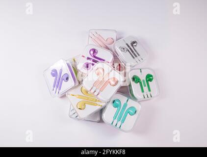 Auricolari multicolore in scatole poggiate su uno sfondo piatto di superficie bianca. Idea musicale. Concetto di partito astratto e tecnologia minimo. Foto Stock