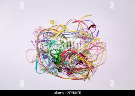Auricolari multicolore aggrovigliati su fondo piatto di superficie bianca. Idea musicale. Concetto di partito astratto e tecnologia minimo. Foto Stock
