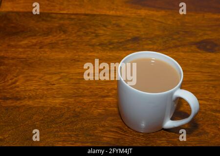 Tè Assam preparato con latte servito in una tazza di ceramica bianca su un tavolo di legno Foto Stock