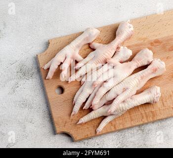 Piedi di pollo grezzi su un tagliere rettangolare di legno su uno sfondo grigio chiaro. Vista dall'alto, disposizione piatta Foto Stock