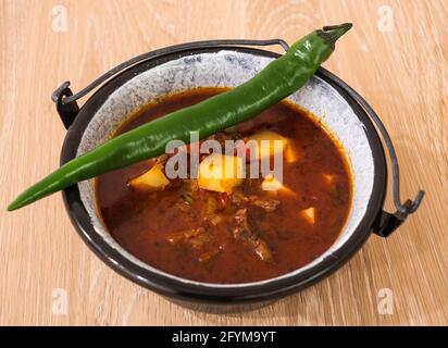 Goulash di manzo ungherese o zuppa di Gulyas o stufato serviti in un piccolo calderone con patate, carne, paprika e peperoncino verde Foto Stock