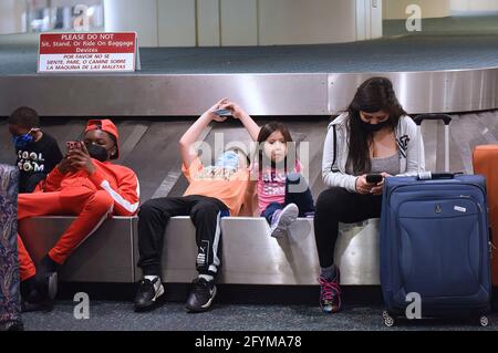 Orlando, Stati Uniti. 28 maggio 2021. I giovani viaggiatori si siedono su un carosello bagagli dopo essere arrivati all'Aeroporto Internazionale di Orlando il venerdì prima del Memorial Day. Dal momento che sempre più persone hanno ricevuto il vaccino COVID-19, l'American Automobile Association (AAA) prevede che oltre 37 milioni di americani percorreranno più di 50 miglia questo fine settimana del Memorial Day, molti per la prima volta dall'inizio della pandemia. Credit: SOPA Images Limited/Alamy Live News Foto Stock