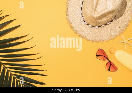 Foglia di palma, crema solare, cappello, occhiali da sole e stelle marine su sfondo giallo con spazio per la copia al centro. Foto Stock