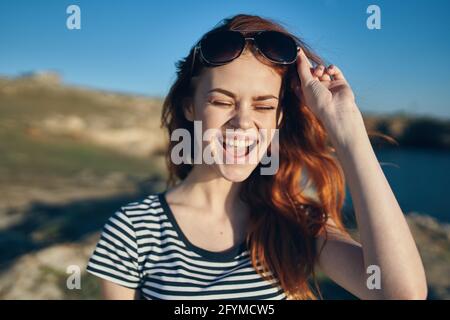 donna allegra che indossa occhiali da sole montagne all'aperto vicino al mare Foto Stock