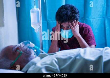 Preoccupato ha sottolineato il giovane uomo a causa di suo padre covid 19 infezione e respirazione su maschera di ossigeno del ventilatore in ospedale - concetto di malattia mentale su Foto Stock