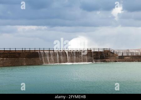 Paesaggio costiero con le onde che si affacciano su una parete di cemento in mare aperto sotto il cielo nuvoloso. Alessandria, Egitto Foto Stock