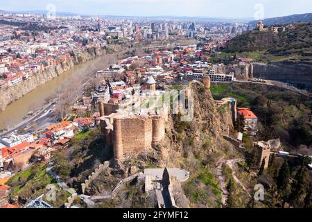 Vista panoramica dal drone dei quartieri storici di Tbilisi sulle rive del fiume Mtkvari e mura medievali della fortezza Narikala su ripida collina in primo piano Foto Stock