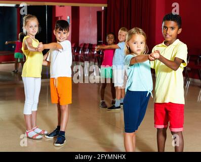 Gruppo di felici e allegri bambini sorridenti che cercano di ballare con il compagno in classe Foto Stock