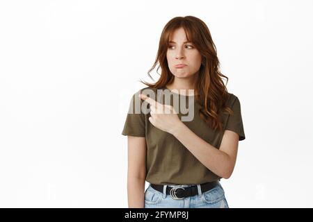 La ragazza sconvolta mostra la cosa ingiusta, puntando e guardando a sinistra con la faccia triste sulking, lamentandosi, fissando con espressione delusa gelosa, in piedi Foto Stock