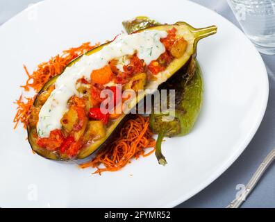 Gustose grigliate di metà di melanzane con ripieno di verdure al forno servito con salsa tzatziki Foto Stock