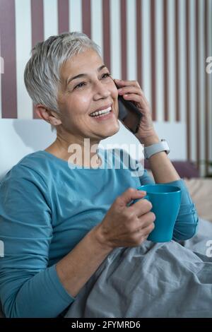 Donna che usa lo smartphone a letto Foto Stock