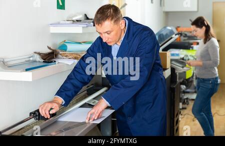 L'addetto alla stampa taglia la carta su una taglierina a rulli Foto Stock