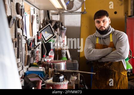 Giovane professionista sicuro fabbro in piedi in officina di lavorazione dei metalli Foto Stock