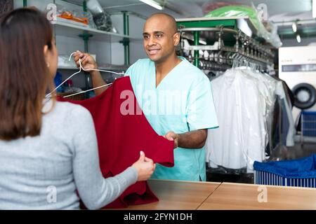 Smilante uomo drycleaner dando capi puliti al cliente, soddisfatti della qualità Foto Stock