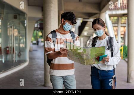 Viaggi, uomo e donna stanno leggendo carta mappa. Indossando maschera, portare zaini e bagagli. Maglietta spogliata e occhiali. Foto Stock