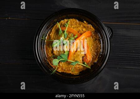 Hummus guarnito con peperoni ed erbe in piastra nera sopra tavolo di legno scuro Foto Stock