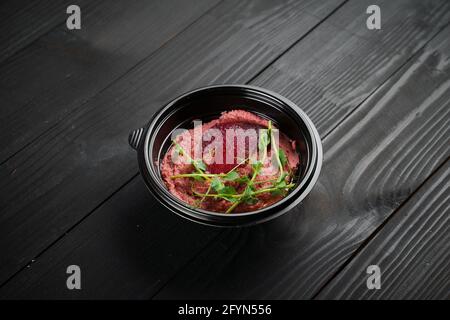 Hummus di barbabietola guarnito con erbe in ciotola nera su tavola di legno scuro. Foto Stock