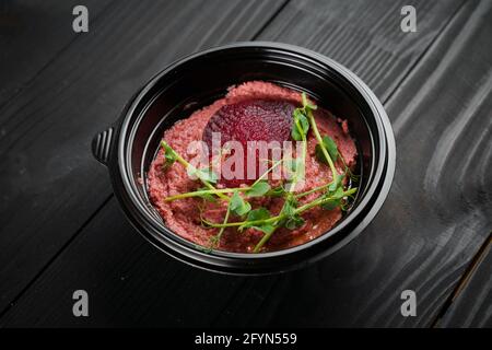 Hummus di barbabietola guarnito con erbe in ciotola nera su tavola di legno scuro. Foto Stock