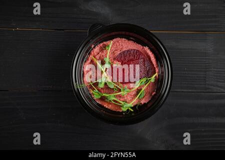 Hummus di barbabietola guarnito con erbe in ciotola nera su tavola di legno scuro. Foto Stock