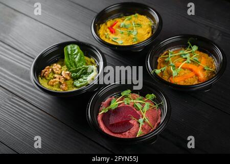 Peperoni, peperoncini, barbabietole ed erbe ummus guarniti in ciotola nera su tavolo di legno scuro. Assortimento hummus. Foto Stock