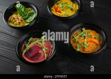 Peperoni, peperoncini, barbabietole ed erbe ummus guarniti in ciotola nera su tavolo di legno scuro. Assortimento hummus. Foto Stock