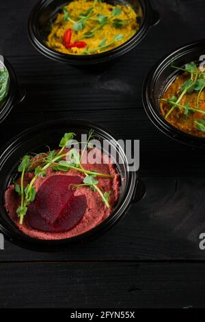 Peperoni, peperoncini, barbabietole ed erbe ummus guarniti in ciotola nera su tavolo di legno scuro. Assortimento hummus. Foto Stock