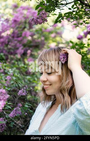 Ritratto autentico candido degli anni '40 della donna bionda caucasica con fiori di lilla. donna di 30 40 anni godendo la vita in fiori lilla sfondo natura Foto Stock