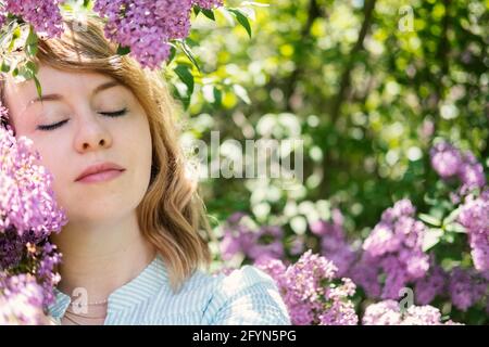 Ritratto autentico candido degli anni '40 della donna bionda caucasica con fiori di lilla. donna di 30 40 anni godendo la vita in fiori lilla sfondo natura Foto Stock