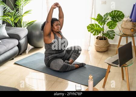 Giovane donna curvy africana facendo pilates classe di idoneità in linea con Laptop a casa - Sport benessere persone stile di vita concetto Foto Stock