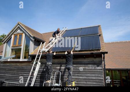 Ingegnere del riscaldamento che installa tubi di raccolta solare-termici evacuati a sud Di fronte al tetto di Ecofhouse in Cotswolds UK Foto Stock