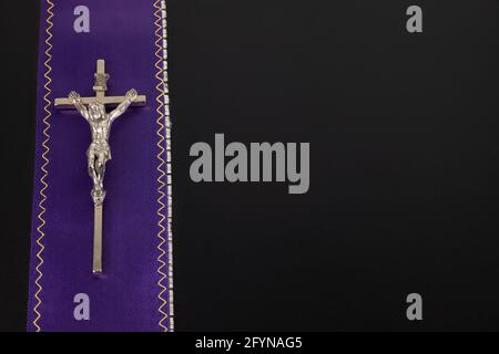 Viola viola stola del sacerdote con una croce di metallo su a. sfondo nero Foto Stock