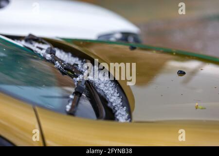 piccole palle di ghiaccio grandine sul cappuccio giallo dell'auto dopo una forte tempesta estiva con messa a fuoco selettiva alla luce del giorno. Foto Stock