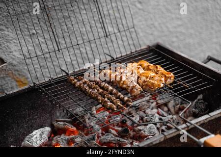 Carne grigliata su spiedini di legno su griglia di metallo su carbone. Cottura di pollo, cuori Foto Stock