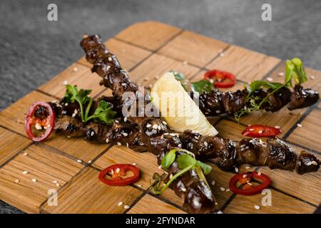 Cuori di pollo grigliati con lime su spiedino di legno, guarniti con peperoncino, coriandolo, sesamo su sfondo grigio Foto Stock