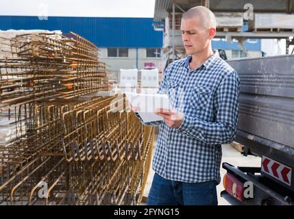 Commissionatore giovane con carte che raccolgono prodotti nel magazzino dei materiali da costruzione Foto Stock