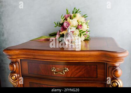 Anelli di nozze con profumo e un bouquet di nozze sul comodino. Simboli di matrimonio, attributi. Foto Stock