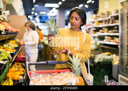 Donna che raccoglie ananas maturo al supermercato della drogheria Foto Stock