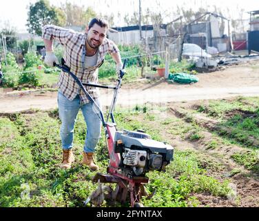 Giardiniere utilizzando coltivatore motorizzato nel suo giardino Foto Stock