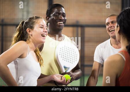 Ritratto di giovane donna paddle tennis giocatore durante allegra conversazione con i suoi amici sul campo indoor dopo la partita Foto Stock